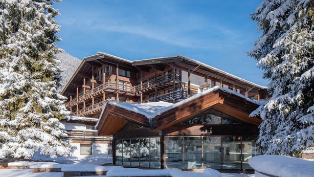 Een houten lodge met een balkon en grote ramen, omringd door met sneeuw bedekte bomen.