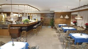 Een restaurant met een bar, diverse zitplaatsen zoals kraamstoelen en tafels, en hangende pendelverlichting.