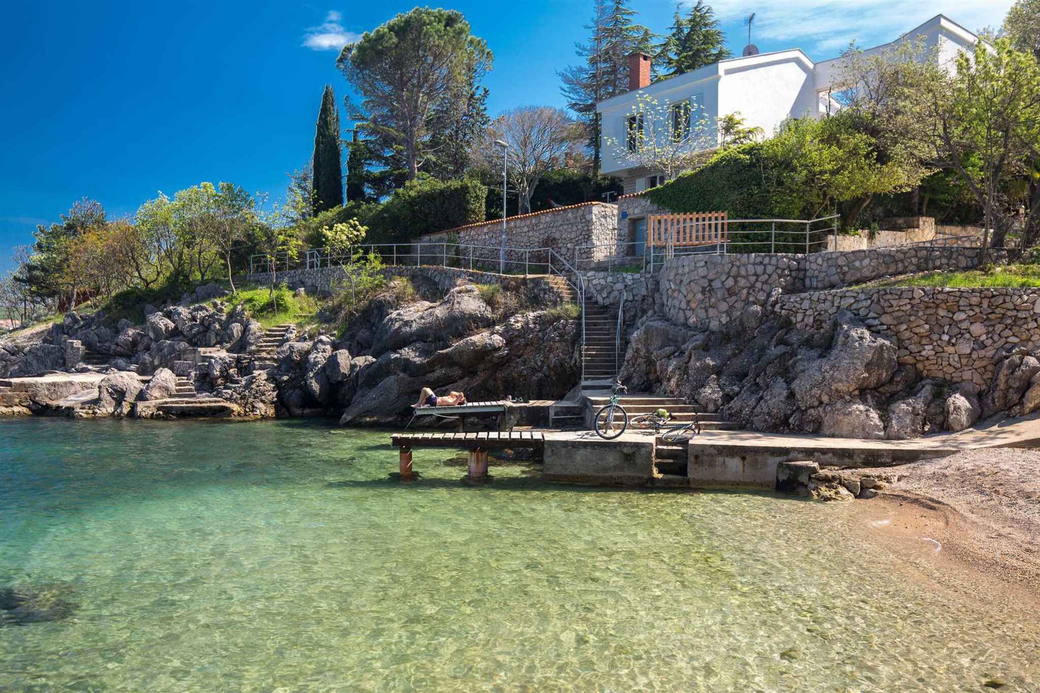En fastighet vid kusten med en pool med klart vatten, trappsteg av sten och en vit byggnad.