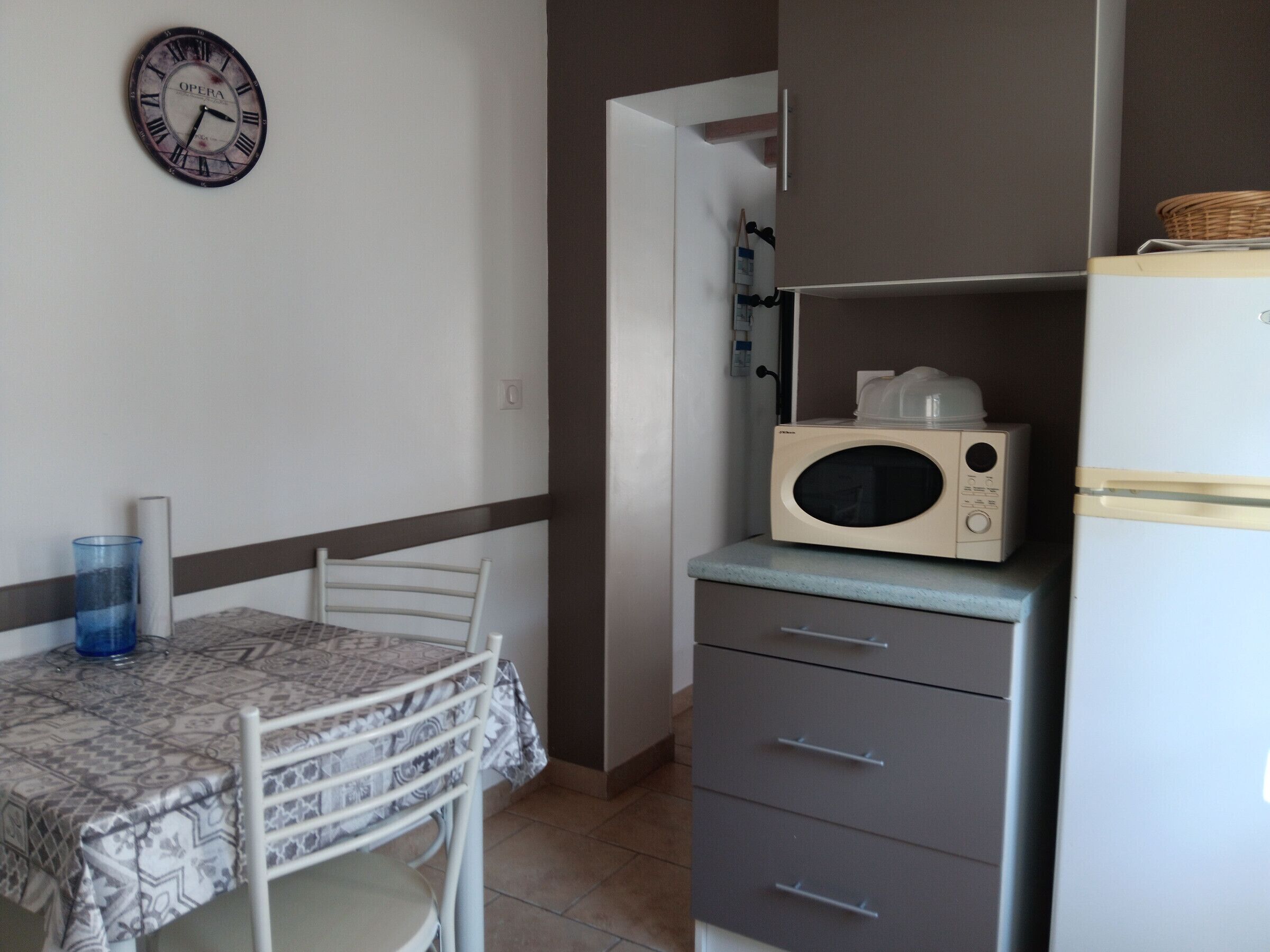 A small kitchen with a microwave, a table with chairs, and a clock on the wall.
