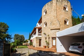 A stone building with a tower, a white car, and a well-maintained garden. - Fantastic Holiday Home with Sea View, Pool, Terrace (Can Furnet, Ibiza)