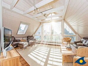 A spacious loft with high ceilings, large windows, and a cozy seating area with leather sofas and a television.