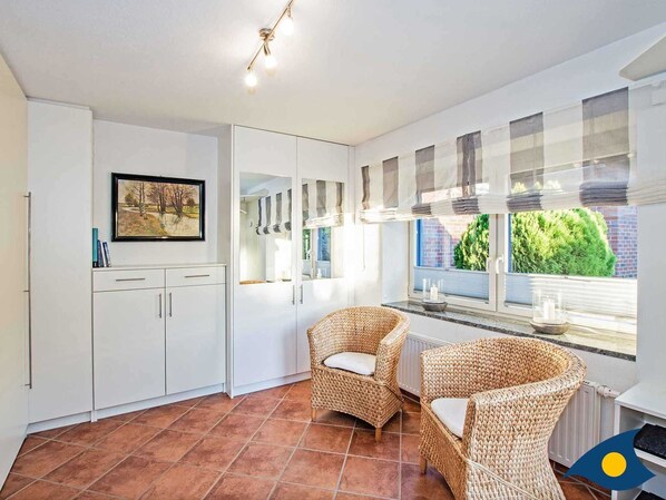 Una cocina moderna con armarios blancos, un comedor con sillas de mimbre y un ventanal con persianas.