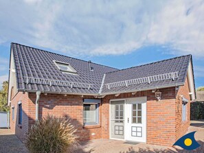 A two-story brick house with a tiled roof, a small attached garage, and a front door with a window.