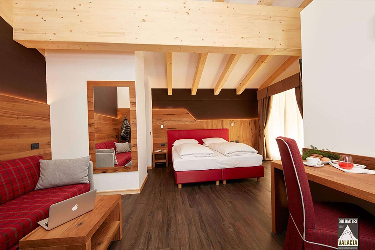 A modern room with a wooden ceiling, a red bed, a wooden desk, and a laptop on a bench.