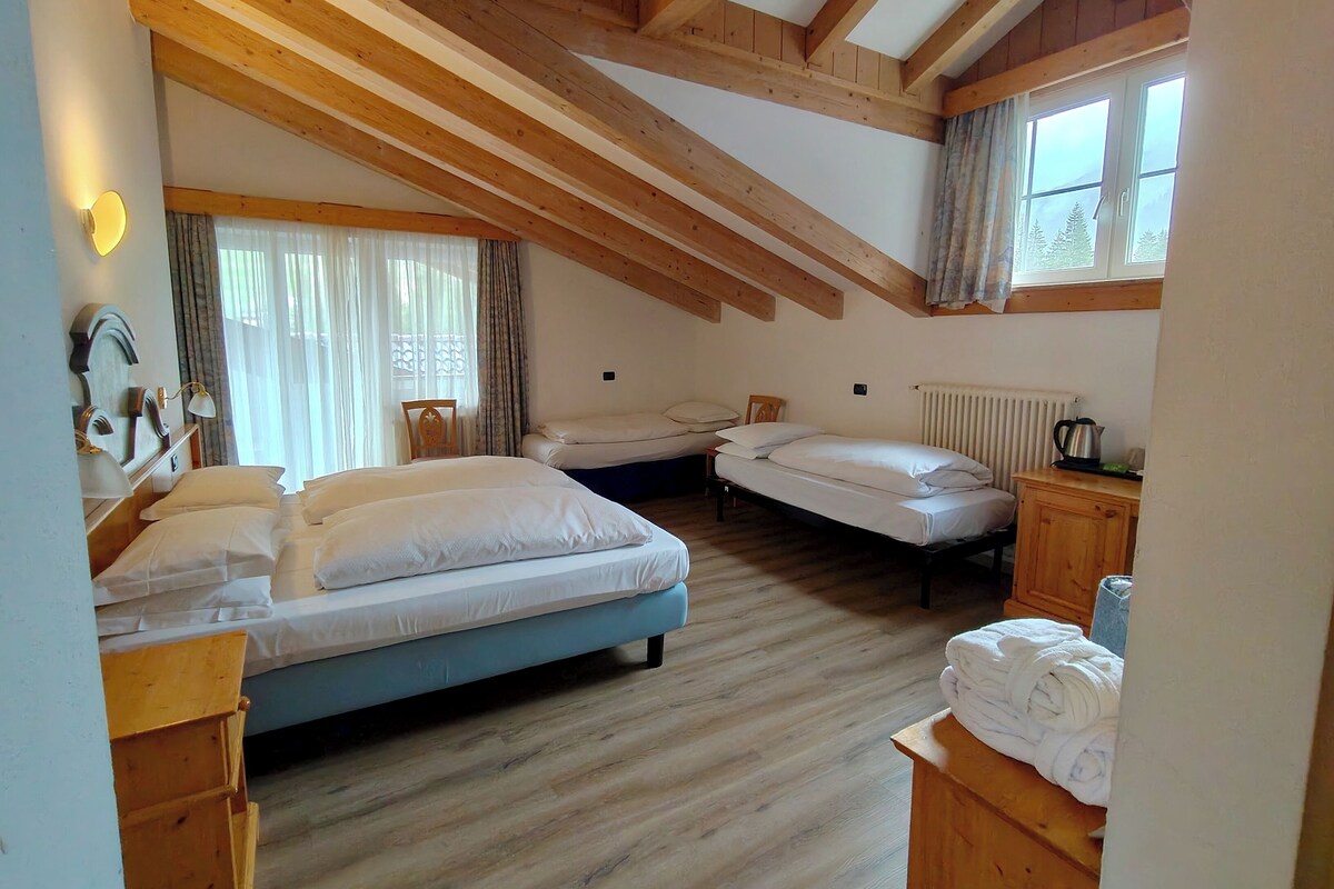 A room with two beds, a wooden ceiling, a radiator, and a window with curtains.