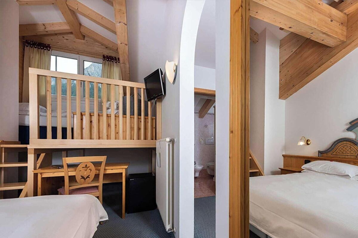 A room with a bunk bed, a desk with a chair, a television, and a bed with a decorative headboard.