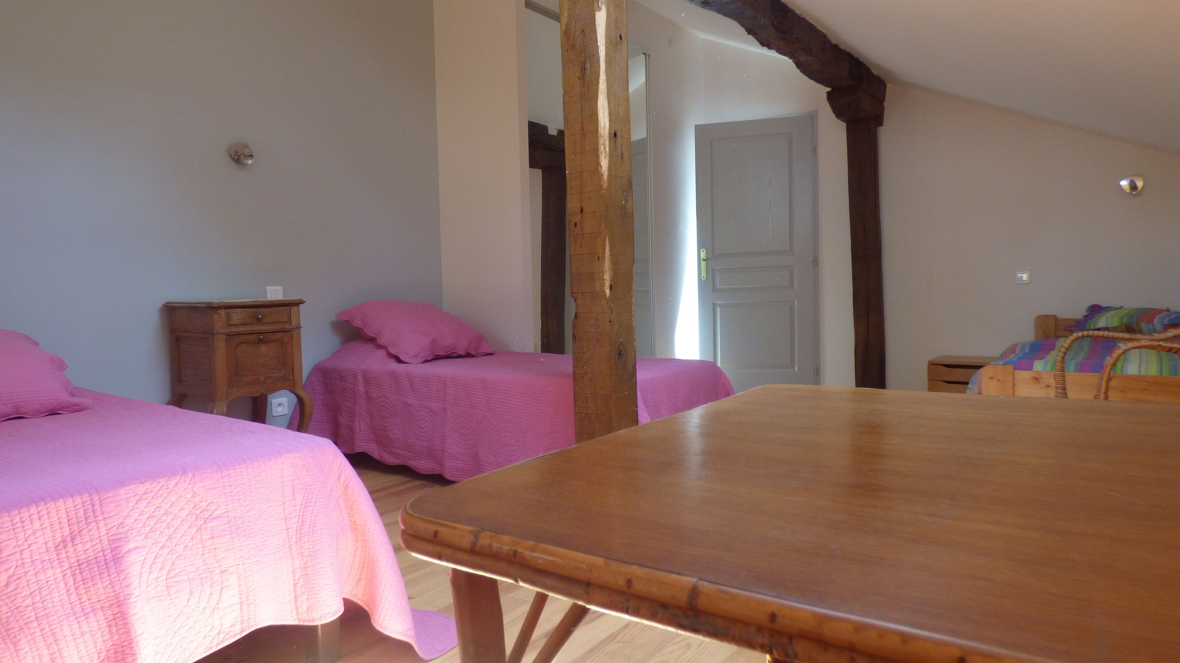 A bedroom with two beds, a wooden table, and a wooden wardrobe.