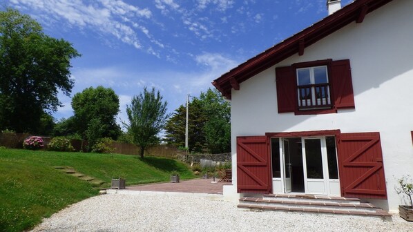 A house with a gravel driveway, a wooden fence, and a grassy area with trees.