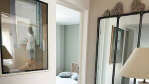 Una camera d'albergo con un letto, uno specchio, una lampada e vista sul mare attraverso una finestra.