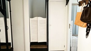 Un corridoio con pavimento in legno, una panca, un appendiabiti con borse e una porta che dà su una stanza con una finestra.