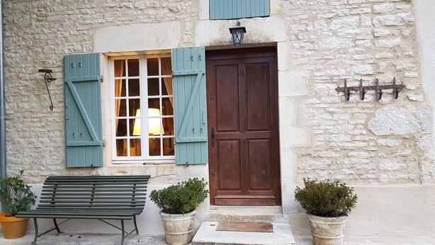 A stone building with a wooden door, a bench, and two potted plants. - Charming renovated farmhouse in Burgundy, near Vezelay. (Chamoux)