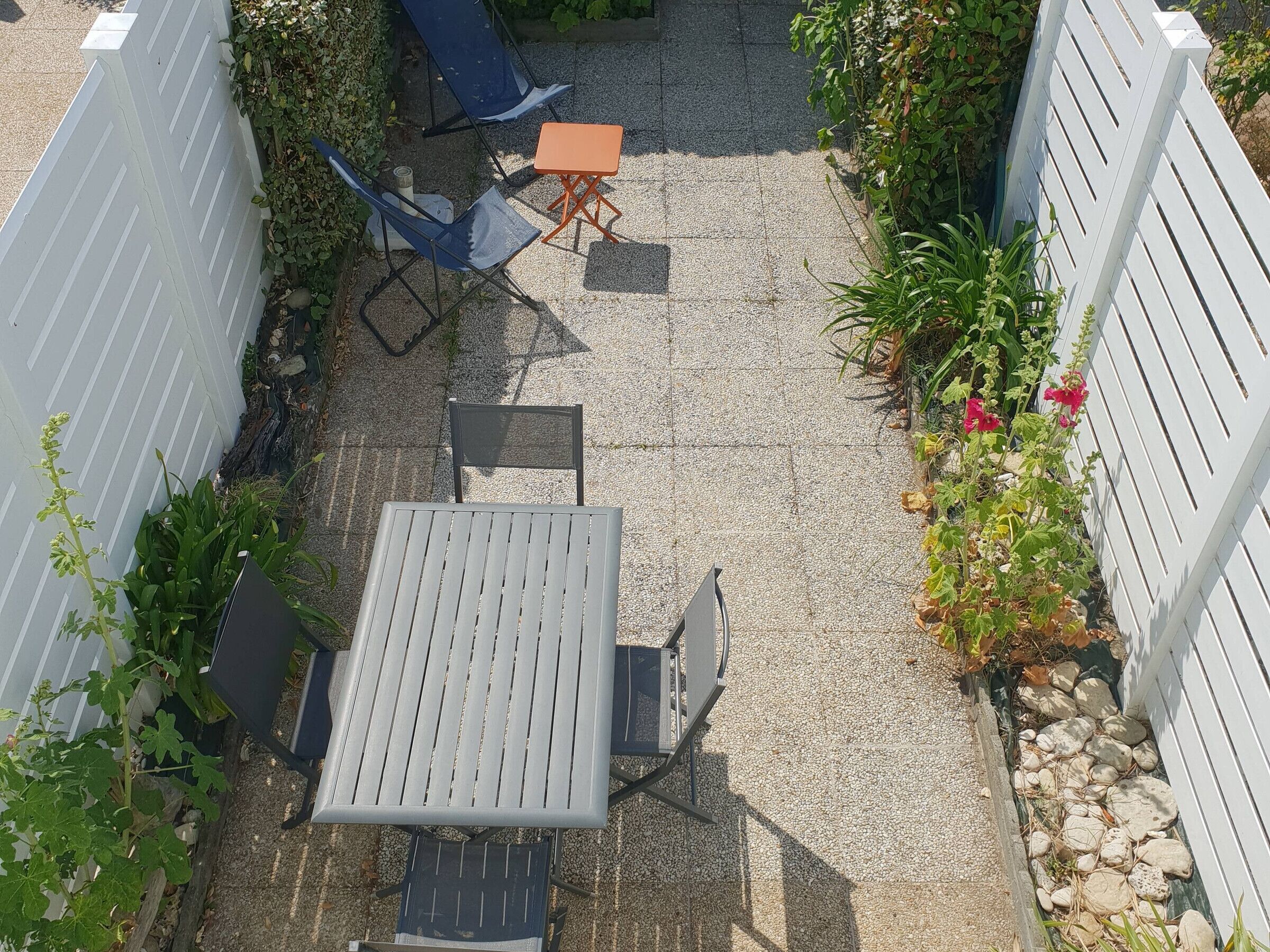 Un patio con mesa y sillas, rodeado por una valla blanca y plantas.