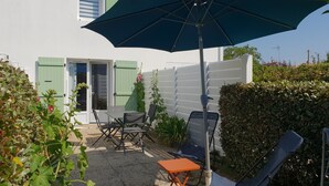A patio with outdoor furniture, a large umbrella, and a white building with green shutters. - Comfortable house, walk to beach and shops, pets allowed upon request (La Faute-sur-Mer)