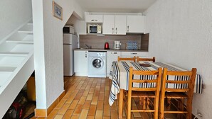 A compact kitchen with a washing machine, microwave, and a small dining area with a table and chairs. - Comfortable house, walk to beach and shops, pets allowed upon request (La Faute-sur-Mer)