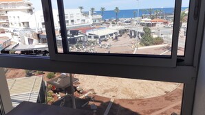 A view from a window overlooking a commercial area with buildings, outdoor seating, and a clear sky. - Studio, 4px, great view of the marina, 66750 St Cyprien beach. 250 € week (Saint-Cyprien)