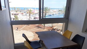 A dining area with a table and chairs, a view of a marina with boats, and a sandy area with palm trees. - Studio, 4px, great view of the marina, 66750 St Cyprien beach. 250 € week (Saint-Cyprien)