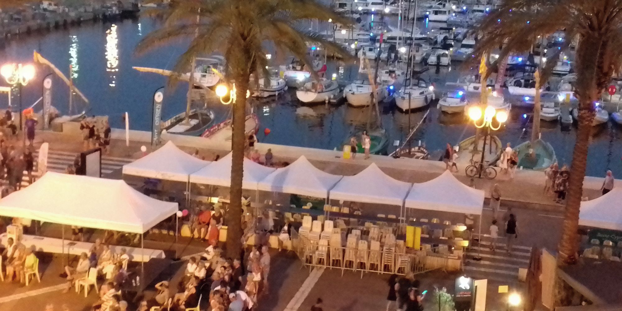 Een jachthaven met afgemeerde boten, mensen in de buurt en tenten voor een evenement.