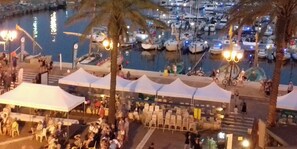 Una marina amb vaixells amarrats, gent reunida i tendes muntades per a un esdeveniment.
