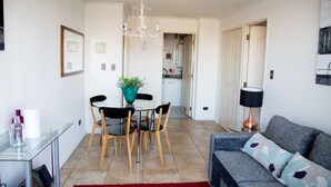 Een moderne woonkamer met een grijze bank, een rood vloerkleed en een eethoek met een glazen tafel en stoelen.