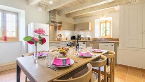 Una cocina moderna con vigas de madera, armarios blancos y una zona de comedor con una mesa de madera preparada para cuatro.