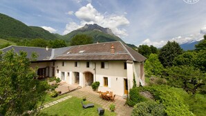 Una cabaña tradicional con un patio de piedra, mobiliario exterior y un paisaje montañoso de fondo.