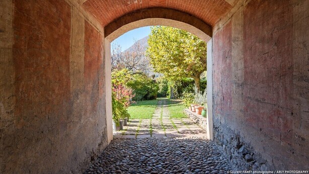 Un corredor de piedra con arco y un sendero adoquinado que lleva a un jardín.