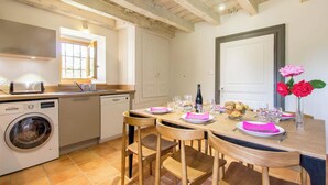 Cocina compacta con lavadora, tostadora y mesa de comedor para cuatro, con servilletas rosas y un florero.