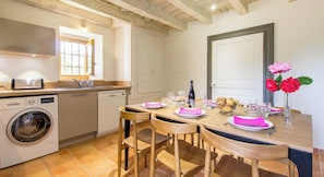 Una cocina compacta con lavadora, una mesa de comedor con sillas y un florero con flores.