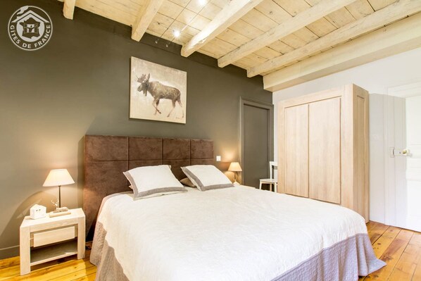 A bedroom with a large bed, wooden headboard, two bedside tables with lamps, a framed picture on the wall, and a wooden wardrobe.