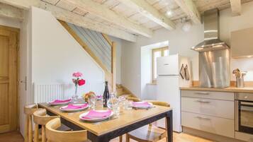 Une cuisine moderne avec une table en bois dressée pour le repas, une hotte de cuisine en acier inoxydable et un réfrigérateur blanc.