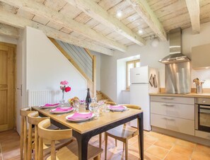 Una cocina moderna con una mesa de madera lista para comer, un extractor de acero inoxidable y un refrigerador blanco.