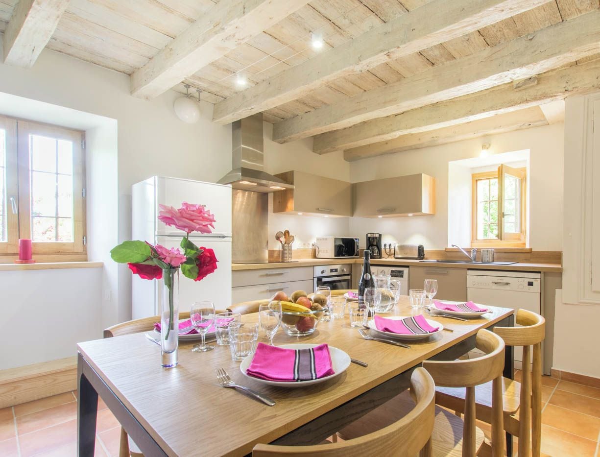 Una cucina moderna con travi in legno, mobili bianchi e un'area pranzo con un tavolo di legno apparecchiato per quattro persone.