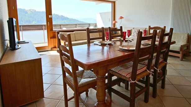 A dining area with a wooden table and chairs, a laptop on a desk, and a view of a lake through large windows. - Stunning 3-room apartment on top floor in Chamrousse (Chamrousse)