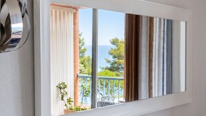 A balcony with a view of the sea and trees, a white wall, and a window with curtains. - Homerez - Sea View Studio - Collioure (Collioure)