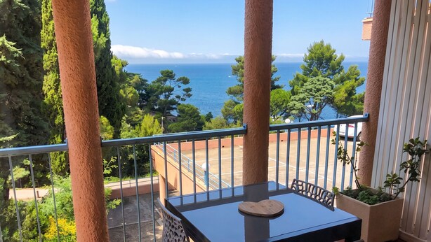 A balcony with a table and chairs, overlooking a coastal area with trees and a view of the sea. - Homerez - Sea View Studio - Collioure (Collioure)