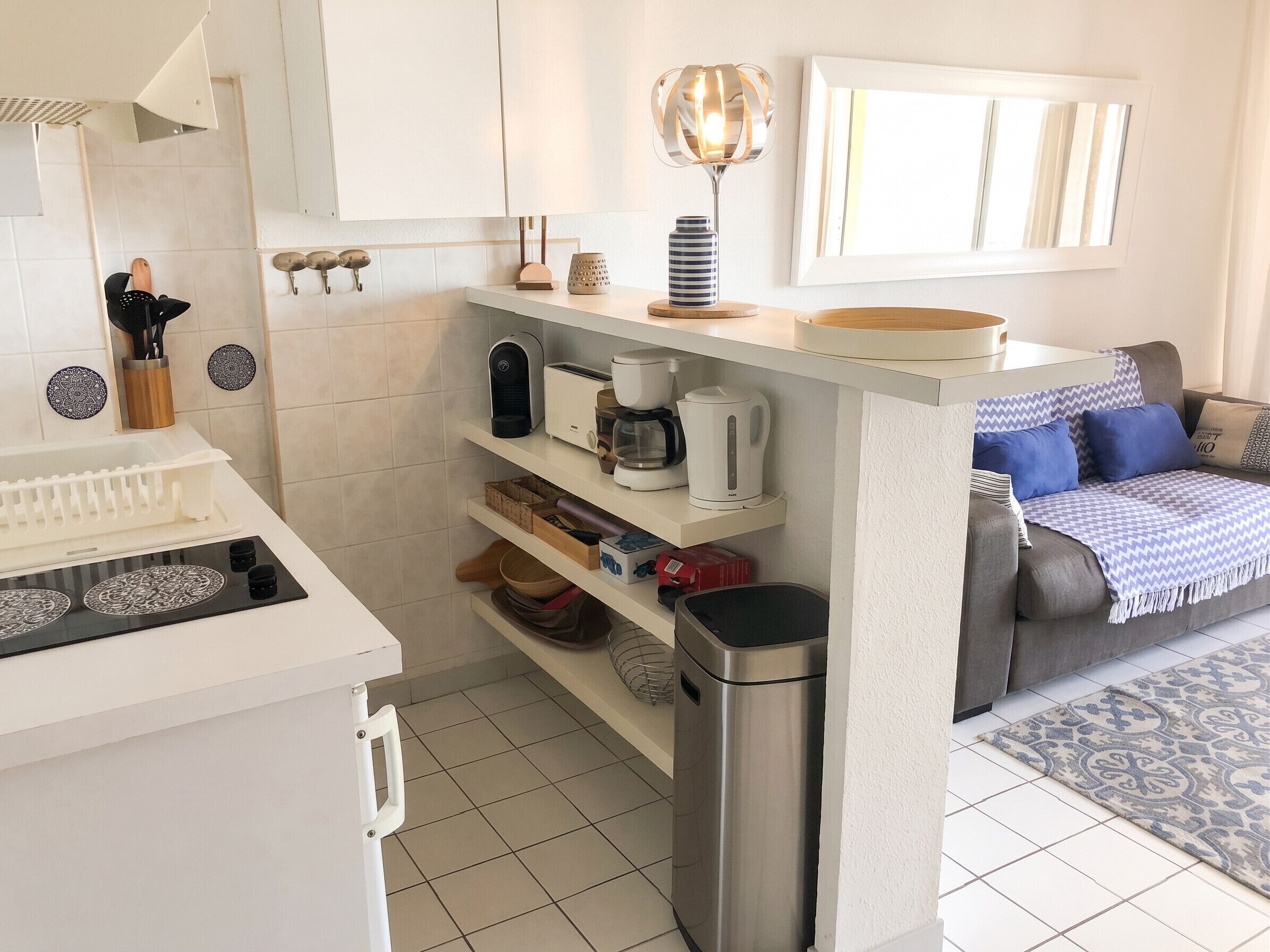 Une cuisine moderne avec des meubles blancs, une machine à café, un grille-pain et une poubelle.