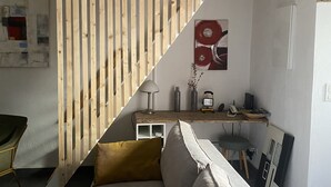 A modern living room with a wooden slatted staircase, a sofa, a desk with a computer, and a small table.