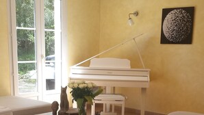 A living room with a piano, a sofa, a coffee table with a vase and a statue, and a wall-mounted lamp. - Charming country house in the middle of the trees private swimming pool gorges de l'hérault  (Causse-De-La-Selle)