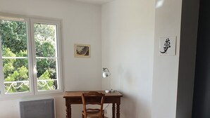 A bedroom with a bed, a desk with a chair, a window with a view of trees, and a radiator. - Charming country house in the middle of the trees private swimming pool gorges de l'hérault  (Causse-De-La-Selle)