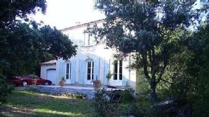 A white building with a tiled roof, surrounded by greenery and a parked red car. - Charming country house in the middle of the trees private swimming pool gorges de l'hérault  (Causse-De-La-Selle)