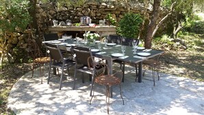An outdoor dining area with a stone wall backdrop, a round table set for six, and metal chairs. - Charming country house in the middle of the trees private swimming pool gorges de l'hérault  (Causse-De-La-Selle)