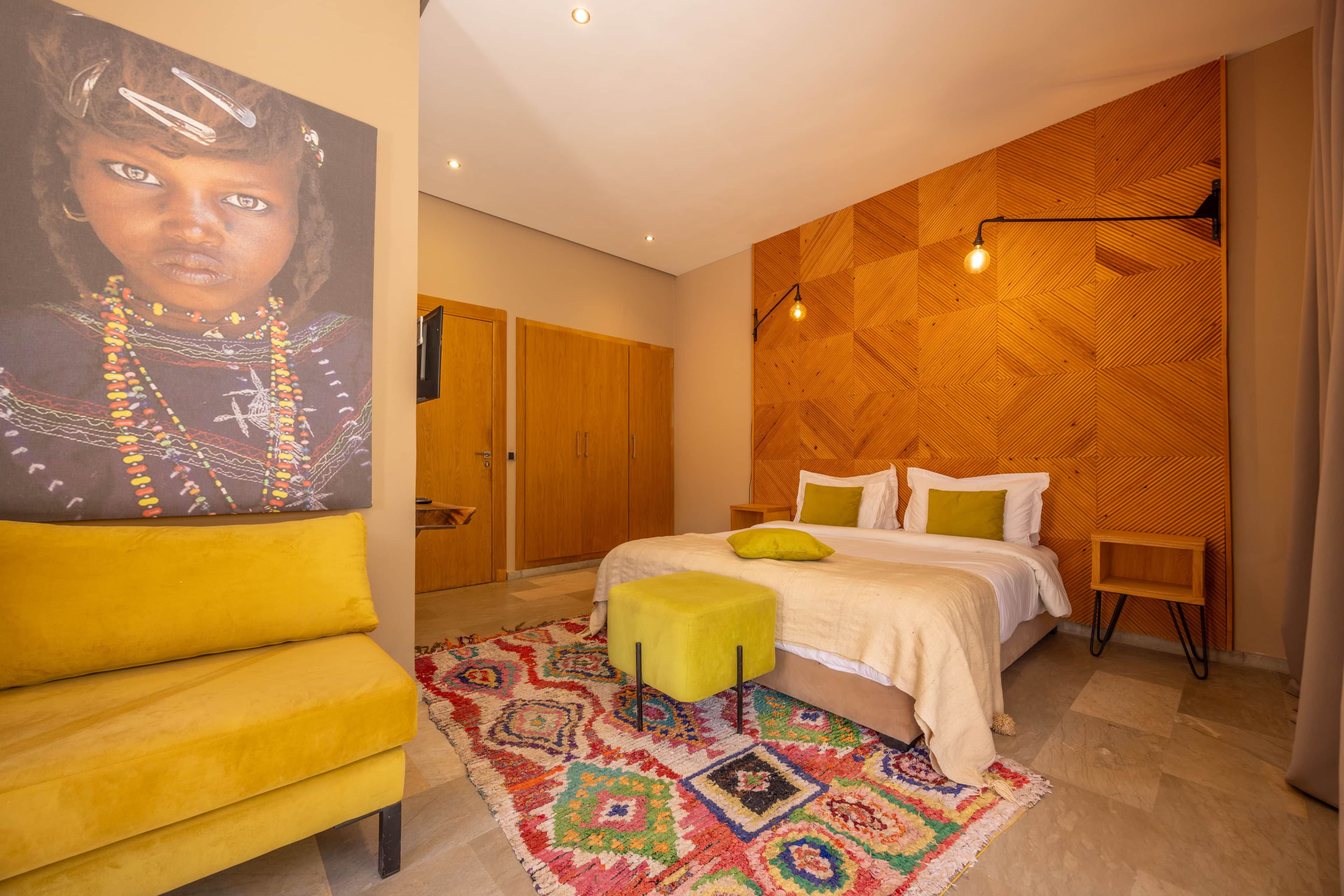 Een slaapkamer met een bed, een gele stoel, een kleurrijk vloerkleed en een houten wandpaneel.