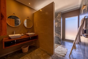 Een moderne badkamer met twee wasbakken, een houten wastafelmeubel, een accentmuur van steen en een groot raam.
