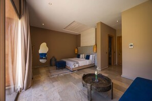 Een slaapkamer met een bed, een ronde bijzettafel, een spiegel en een blauwe stoel.