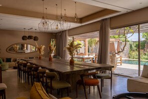 A spacious dining area with a long wooden table, multiple chairs, and hanging pendant lights.