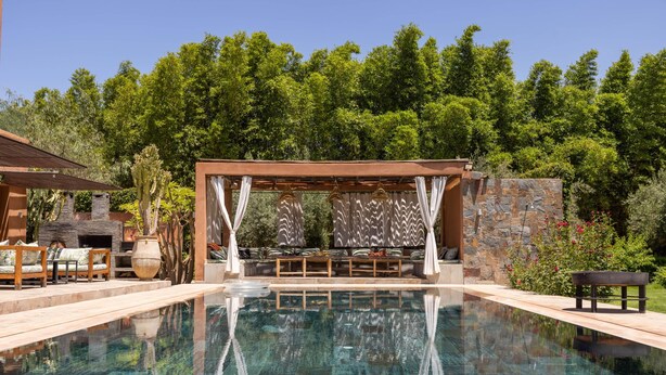 Ein klares Schwimmbecken mit Holzterrasse, Liegestühlen und einer Pergola mit gemusterten Vorhängen.