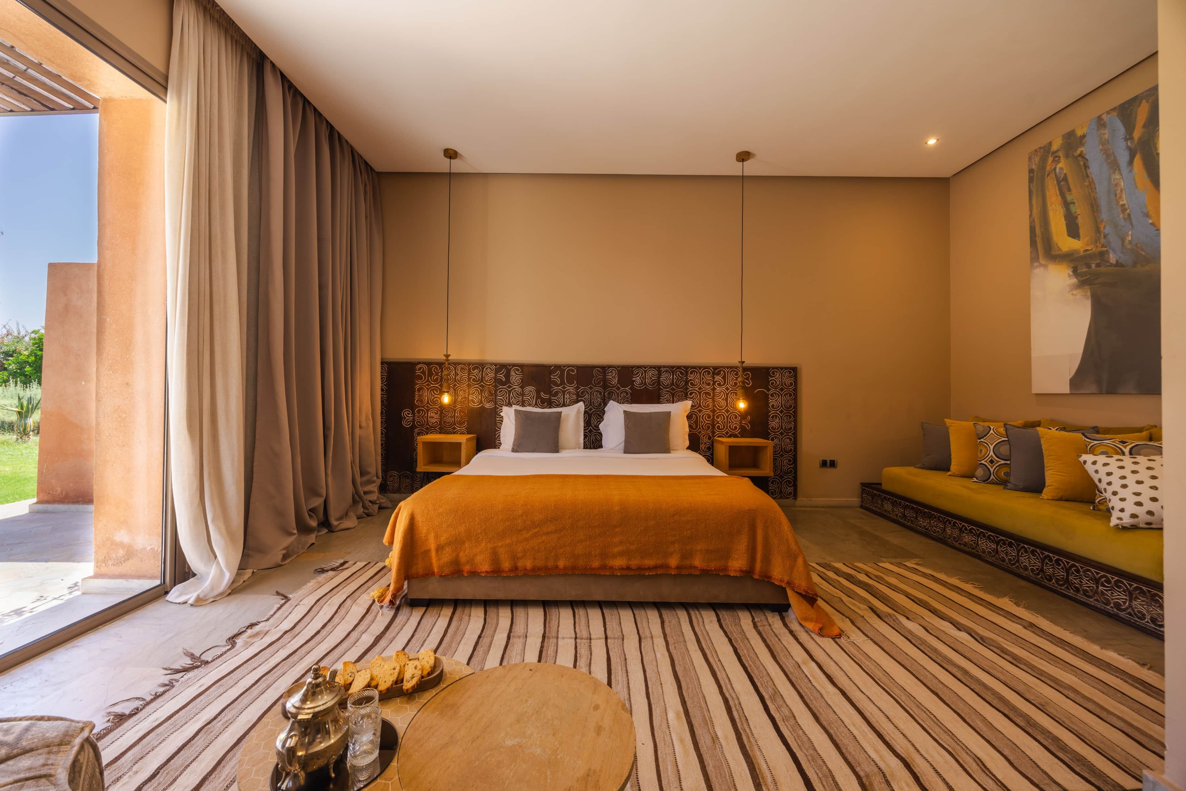 Ein Schlafzimmer mit einem großen Bett, einer Sitzecke, einem Esstisch und Blick ins Freie.