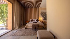 A modern bedroom with a bed, a bench, a nightstand, a large window with curtains, and a cactus outside. - To complete (Marrakech)