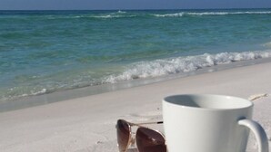 A beach with a white mug and sunglasses on the sand. - Steps from YOUR Balcony to Beach | Excellent Reviews | Beach Service Included (Miramar Beach)